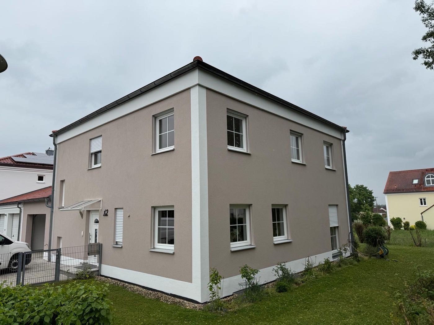 Einfamilienhaus mit Fassade in warmem Greige, weißen Faschen und weißem Sockelband