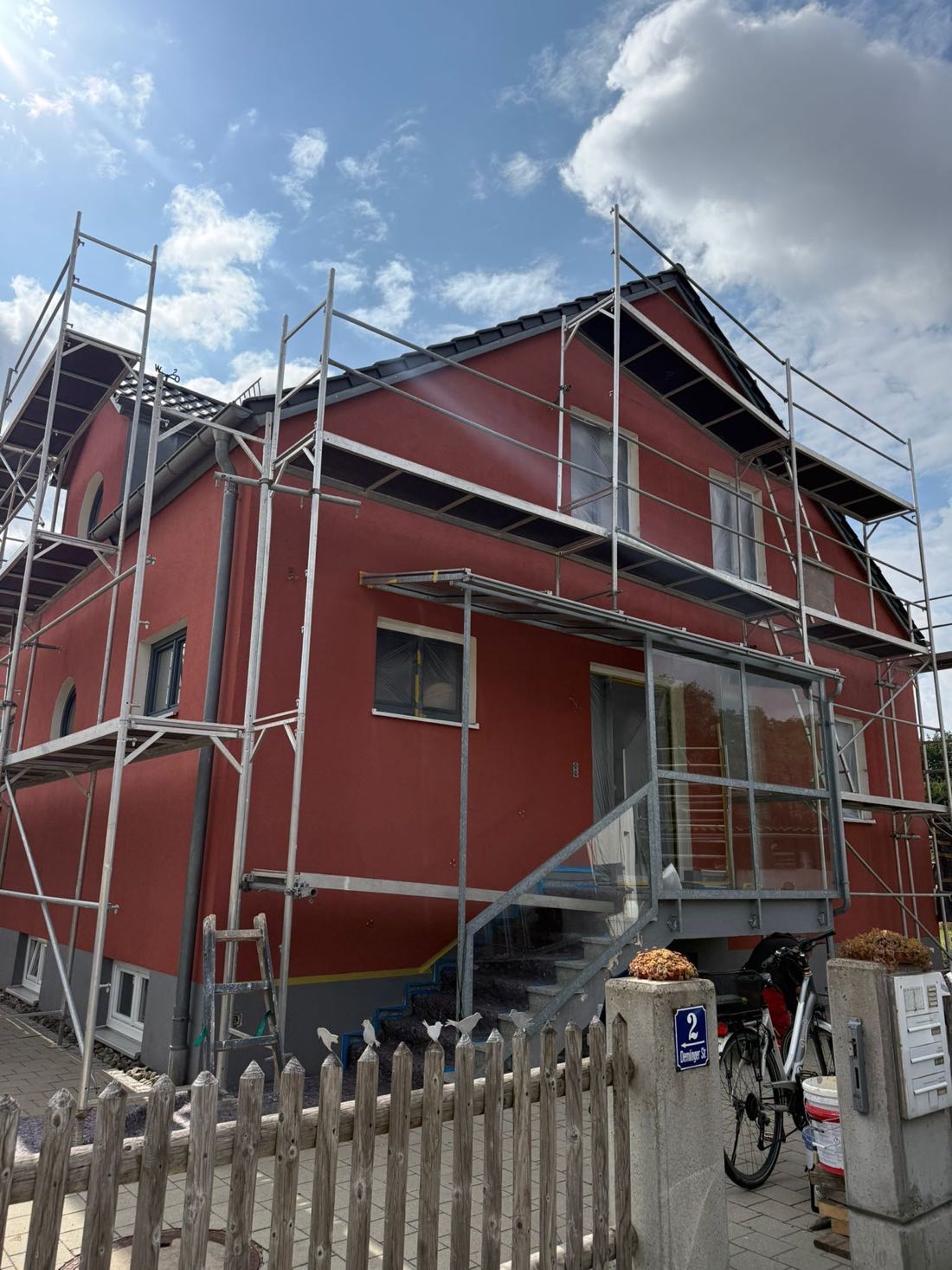 Eingerüstetes Wohnhaus während der Fassadenarbeiten mit frisch aufgetragenem rotem Anstrich