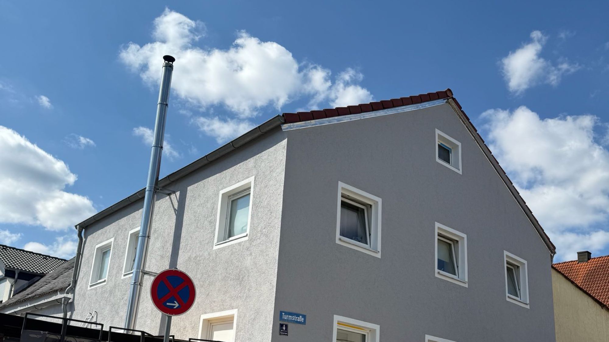 Altbau mit frisch gestrichener Fassade in Hellgrau, weiß abgesetzten Fensterfaschen und blauem Himmel