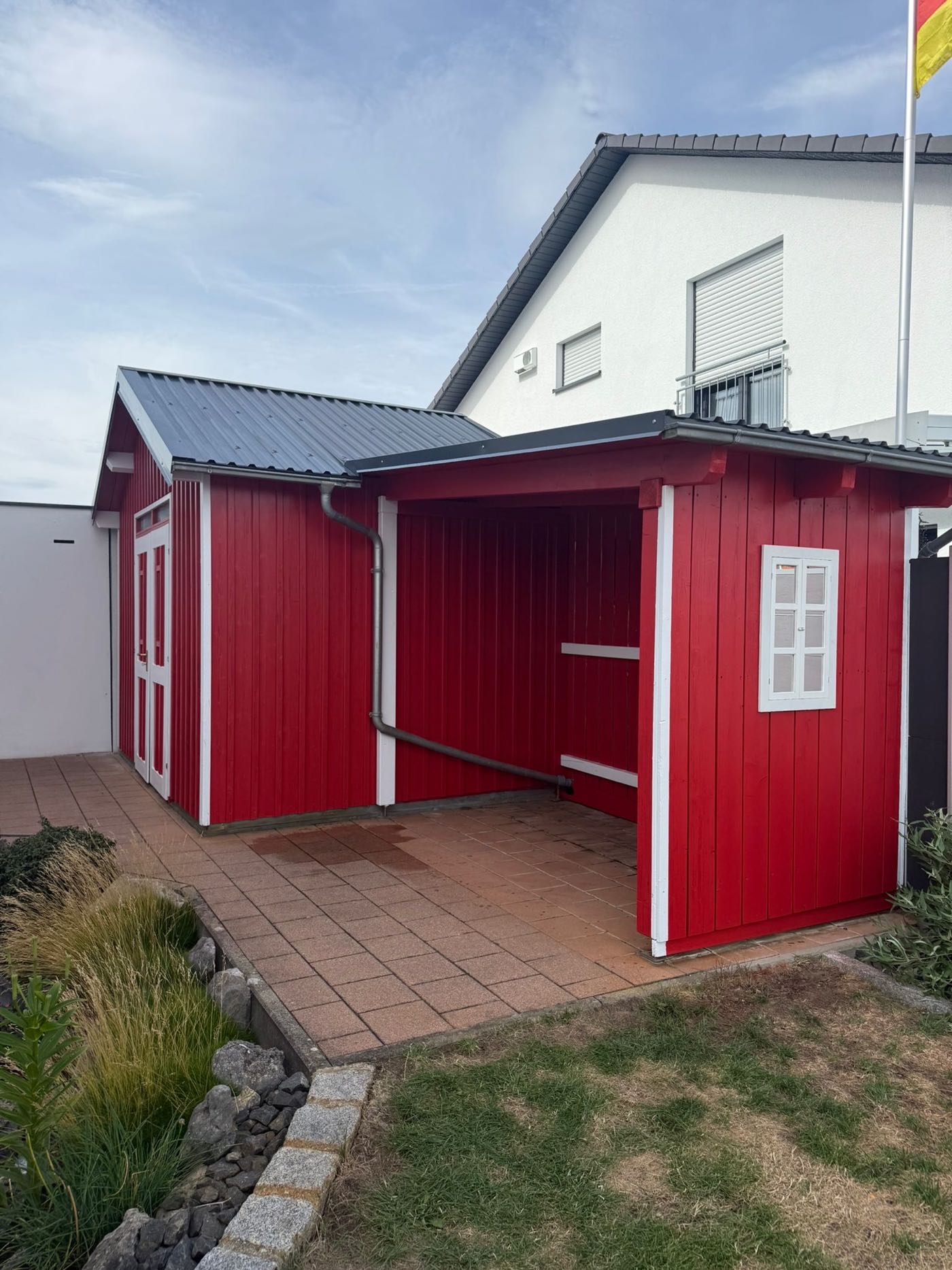 Holzhaus im Garten nach dem Neuanstrich in Rot mit weißen Zierleisten und Türrahmen