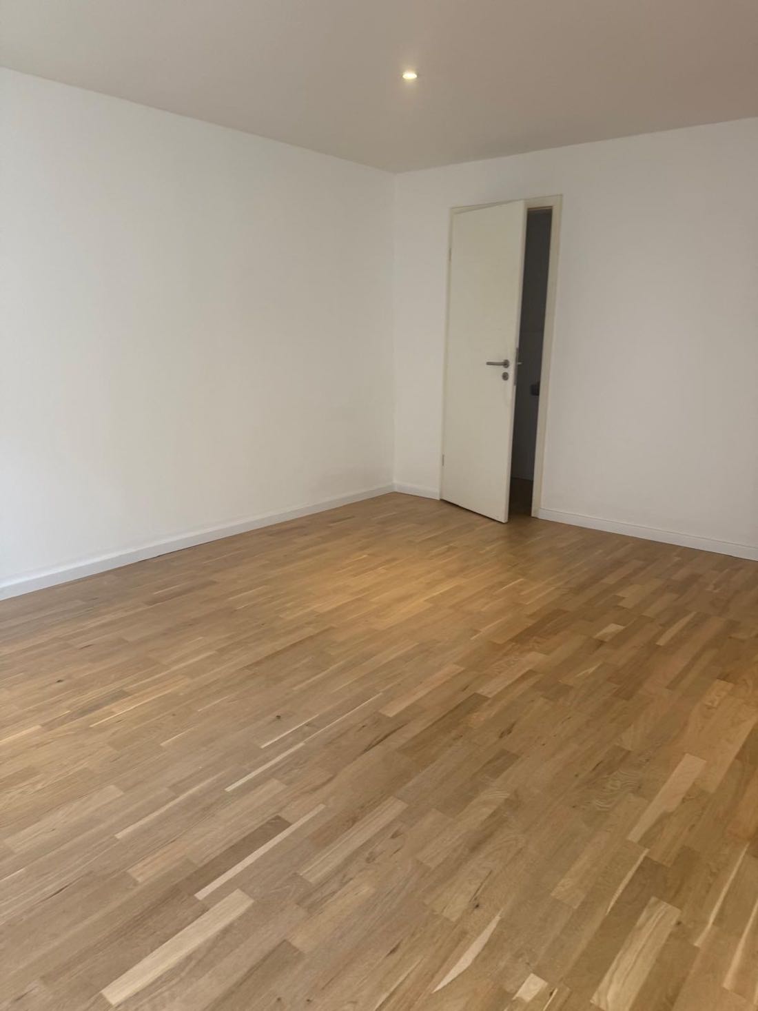 Fertiges Zimmer mit weißen Wänden, weißer Tür und Eichenparkett