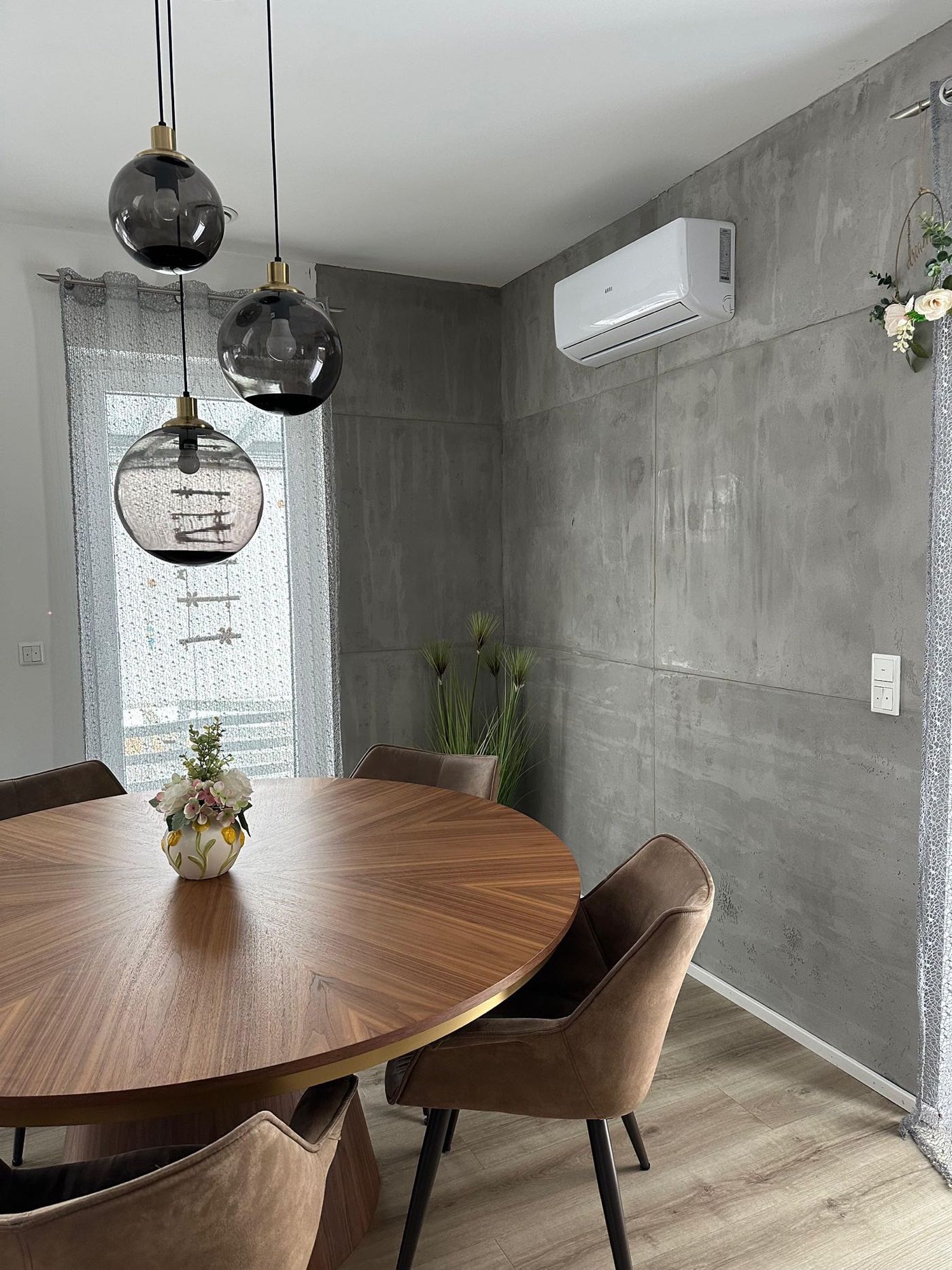 Essbereich mit Wand in Sichtbeton-Optik, rundem Holztisch und Pendelleuchten